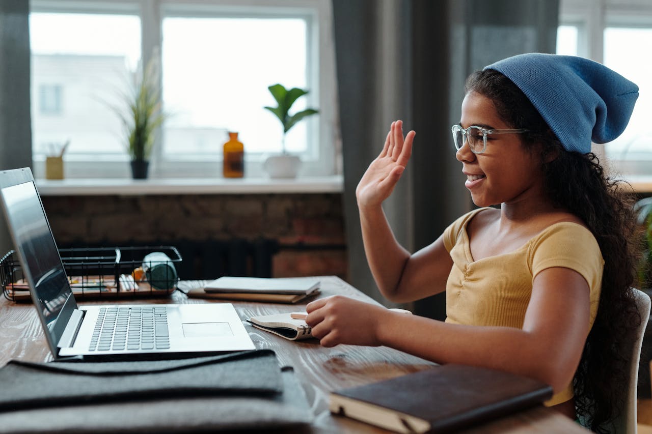 Crafting Captivating Headlines: Your awesome post title goes here A young girl waves at her laptop during a video call in a cozy home office setting.